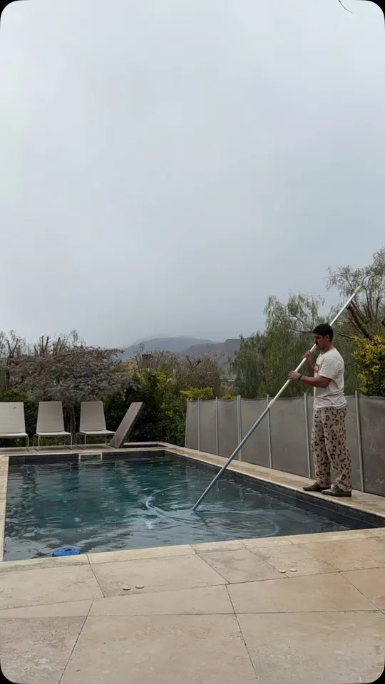 Una persona del equipo pasa el barrefondo por una piscina, con la montaña de fondo